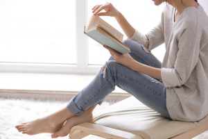 Young woman, sitting on ottoman and reading in a bright room