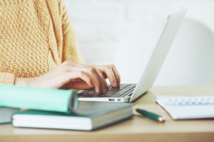 Woman sitting at computer, wearing yellow sweater, books on desk nearby