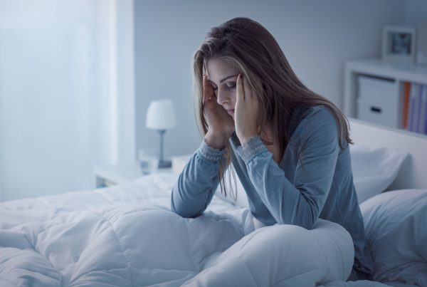 Woman sitting in bed in dark room, hands massaging temples, unable to sleep