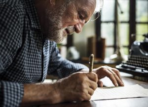 Elderly man handwriting an obituary