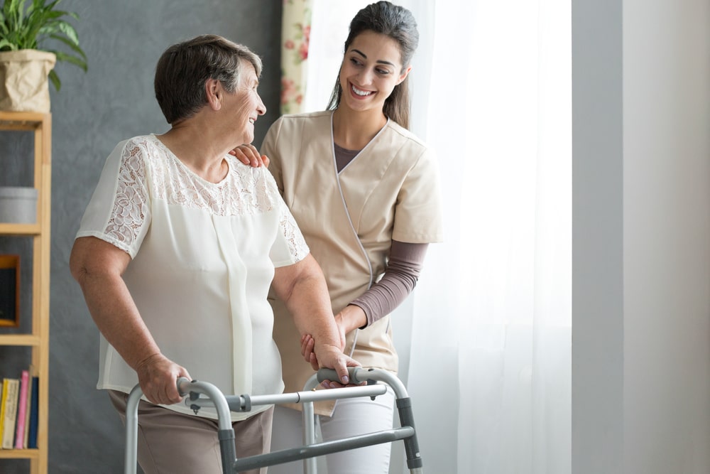 Nurse helping elderly woman move with walker