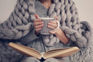 Woman wrapped in cozy blanket while holding mug and looking at photo album