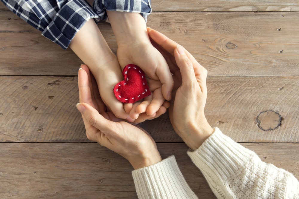 Parent cupping child's hands as child holds a red, cloth heart