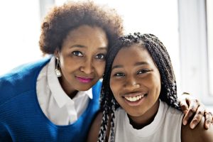 Woman in blue with teenage daughter, both looking into camera