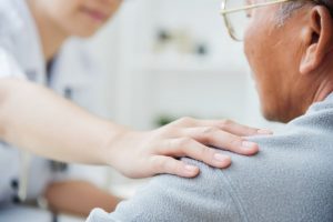 Female nurse putting comforting hand on elderly man's shoulder