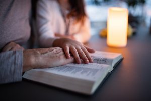 Mom and teenage daughter reading the Bible together, teenager touching mother's hand in a comforting way