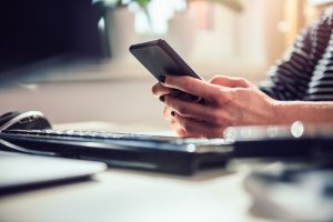 Focus on woman's hands as she holds smartphone with keyboard on table in front of her