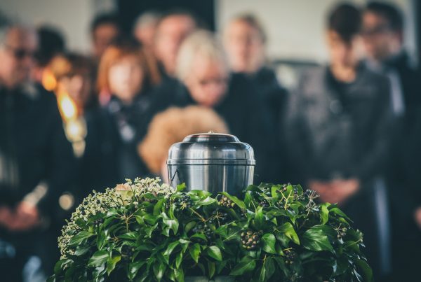 Urn in prominent place, surrounded by greenery, with mourners standing nearby