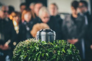 Mourners standing together and looking at a silver urn surrounded by greenery