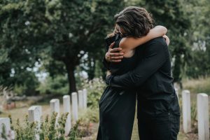 Man and woman wearing black standing in cemetery, hugging and expressing their grief