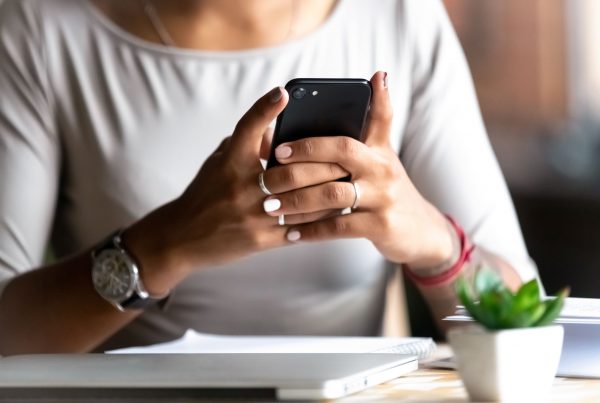 Woman sitting at her desk, holding phone in both hands as she looks at the screen