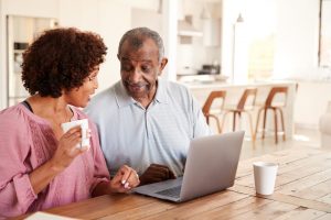 Husband and wife sitting at table in their home, looking at each other, computer in front of them