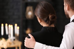 Man and woman standing together, looking at memorial candles, his hand on her shoulder as he offers support