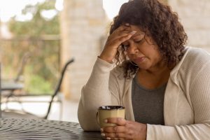 Upset young woman sitting at table, touching forehead and thinking