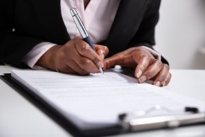 Focus on woman's hands as she signs documents on a clipboard