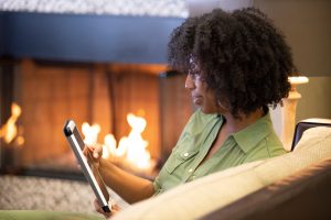 Woman sitting on couch near a fireplace, using her tablet