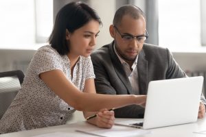 Young man and woman working together on a computer, sitting at table