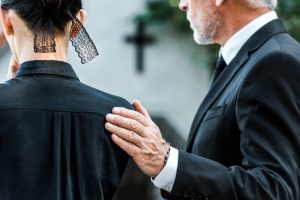 Man and woman wearing black, serious faces, man's hand on woman's shoulder