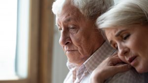 Sad older man and woman, woman laying head on shoulder of man in comfort