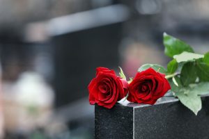 Two red roses lying on top of a dark marble grave markerof 