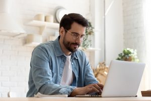 Adult bearded man sitting at table, typing on a computer