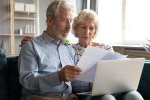 Older husband and wife sitting on couch at home, looking at document and reviewing interment options