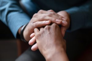 Two people sitting together, one person holding the other person's hand in comfort