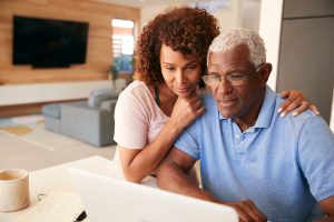 Middle-aged husband and wife sitting at table, looking at computer, reading the screen