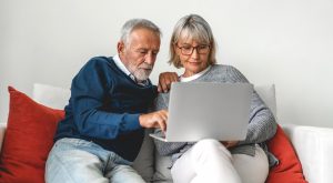 Older husband and wife sitting on red couch while working on a computer together