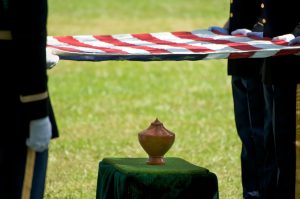 Military personnel holding American flag over urn, getting ready to fold flag