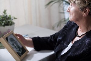 Older woman sitting at table, holding picture of loved one and thinking