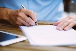 Middle-aged man sitting at table, signing documents, tablet lays nearby