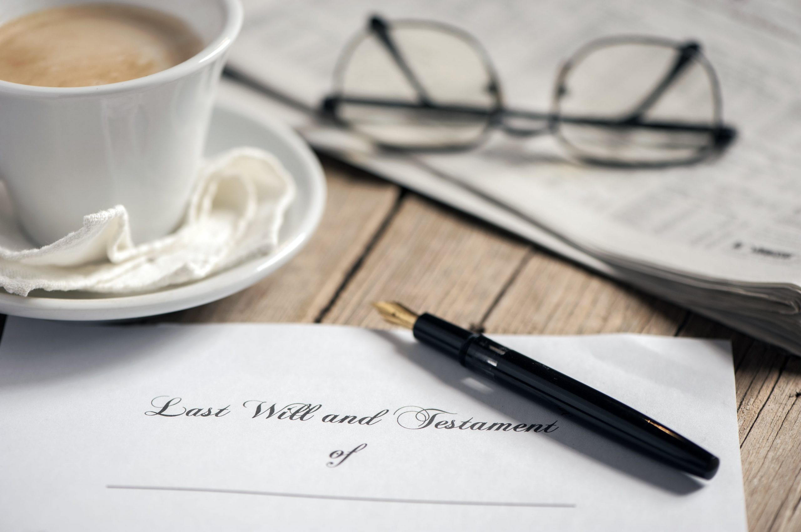 Folded legal will sitting on table near coffee mug, pen, and eyeglasses