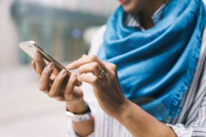 A woman wearing a blue scarf typing on her smartphone