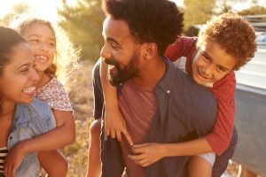 Blended family of 4 outside, mom carrying daughter on back and father carrying son on back