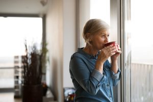 Older woman standing in her home, sipping on a cup of tea, finding a way to move forward and heal