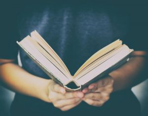 Person wearing dark shirt and holding open book