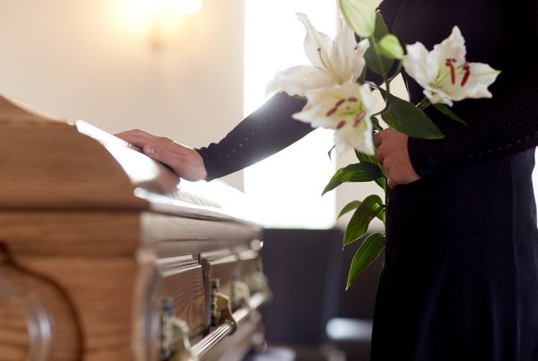 Woman standing next to casket while holding white lilies