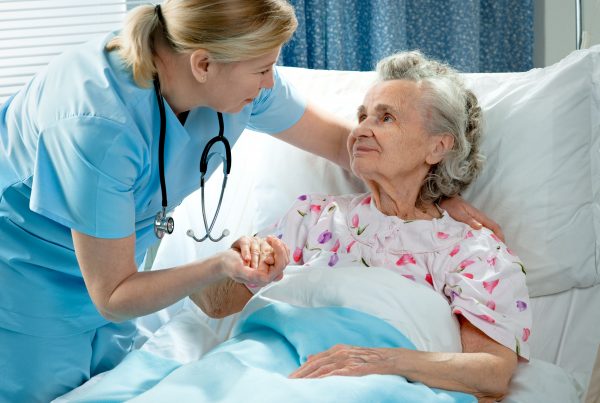 older woman in hospital bed receiving care from nurse