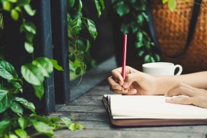 Person sitting outside with a cup of tea and writing in a journal