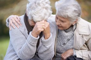 Two mature women sitting together outside, one comforting the other