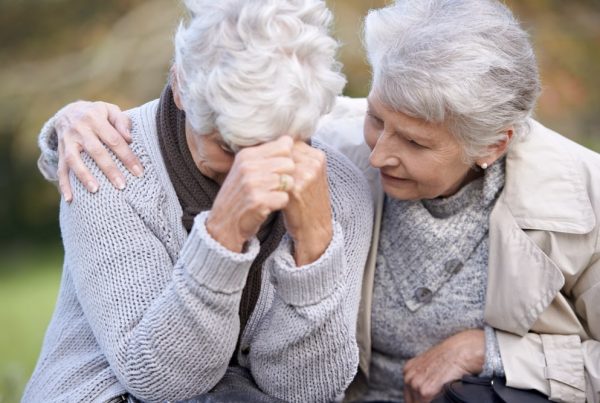 Two mature women sitting together outside, one comforting the other