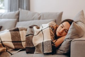 Young woman laying on couch, taking a nap under a cozy blanket