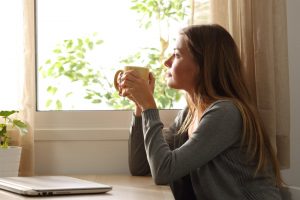 Woman sitting quietly at home with a cup of tea, looking out window and thinking
