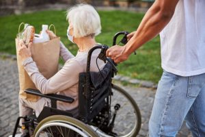 male volunteer pushing an older woman in a wheelchair holding groceries