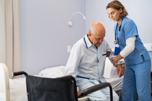 Nurse helping older man get into his wheelchair from the bed