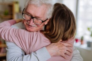 Two people hugging, looking at the face of an elderly man.