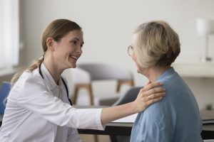 A healthcare professional with her hand on a patient's shoulder offering comfort.
