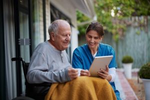 A healthcare worker showing a tablet to an elderly man in a wheelchair.